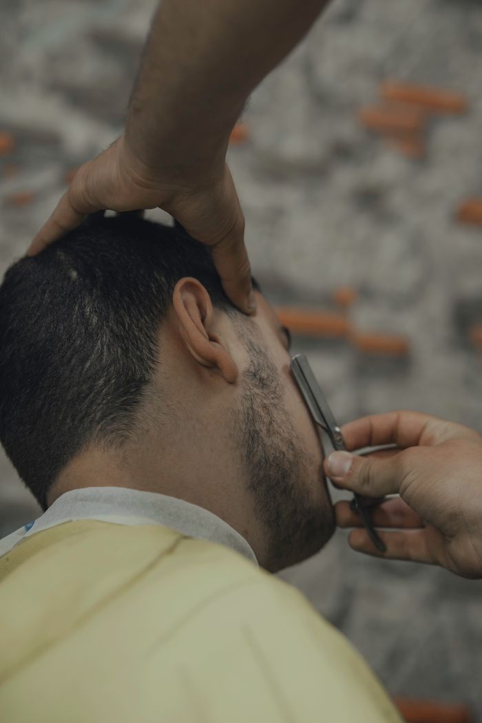 social-feed-img-03 A man getting a close shave with a straight razor at a barbershop.