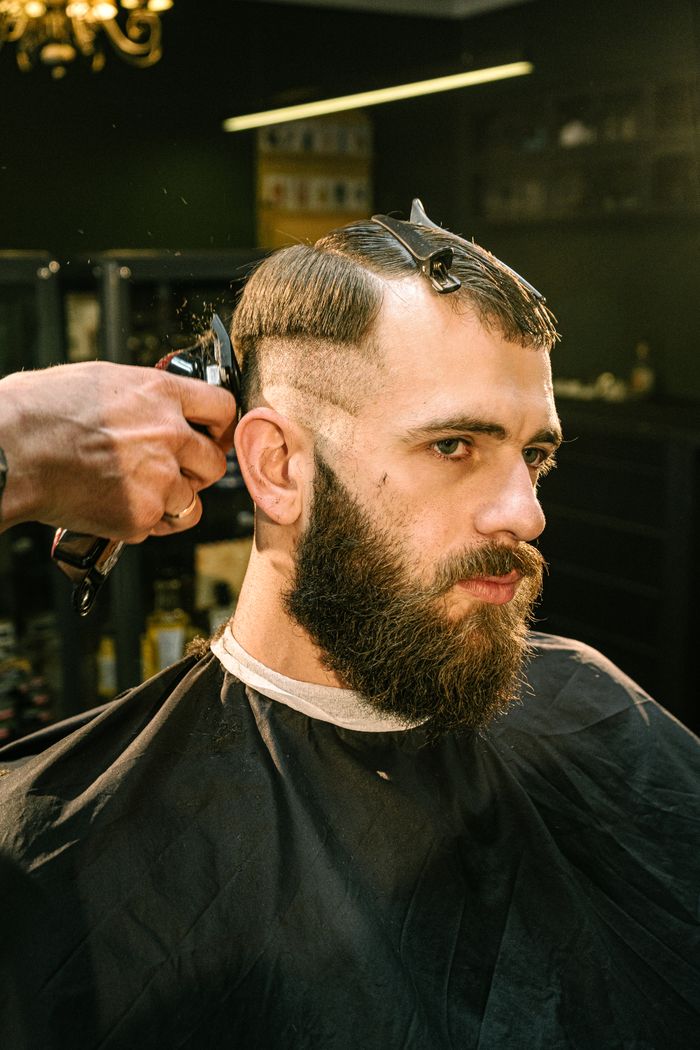 about-img A man receives a haircut and trim in a professional barbershop setting with focus on style and detail.
