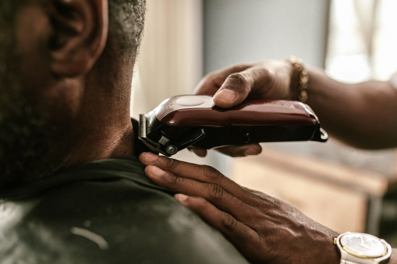 social-feed-img-04 Barber using clippers to trim a client's hair in a barbershop setting.
